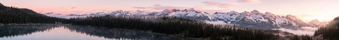 Very wide panorama of a pine forest and a misty lake below a long ridge of snowy peaks lit pink at sunrise, by Nano Banana 2.1 at 8:1