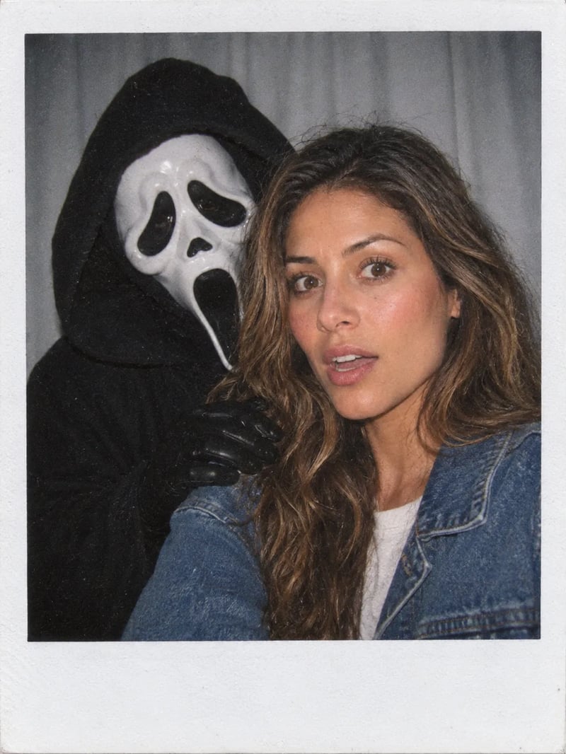 Polaroid of a woman in a denim jacket looking startled while Ghostface leans in behind her