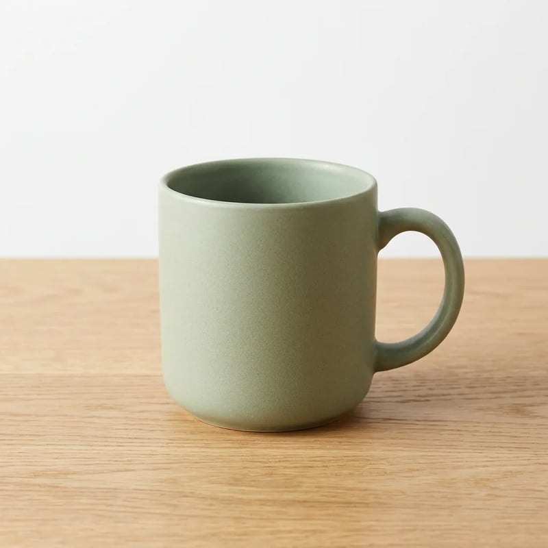 Matte sage green ceramic mug on a light oak table against a plain white wall, soft even light, by Nano Banana 2.1
